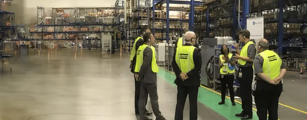 Executives in safety vests wearing headsets on a warehouse tour