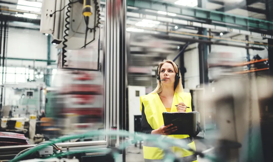 Guide in a safety vest wearing a headset and holding a tablet in a plant