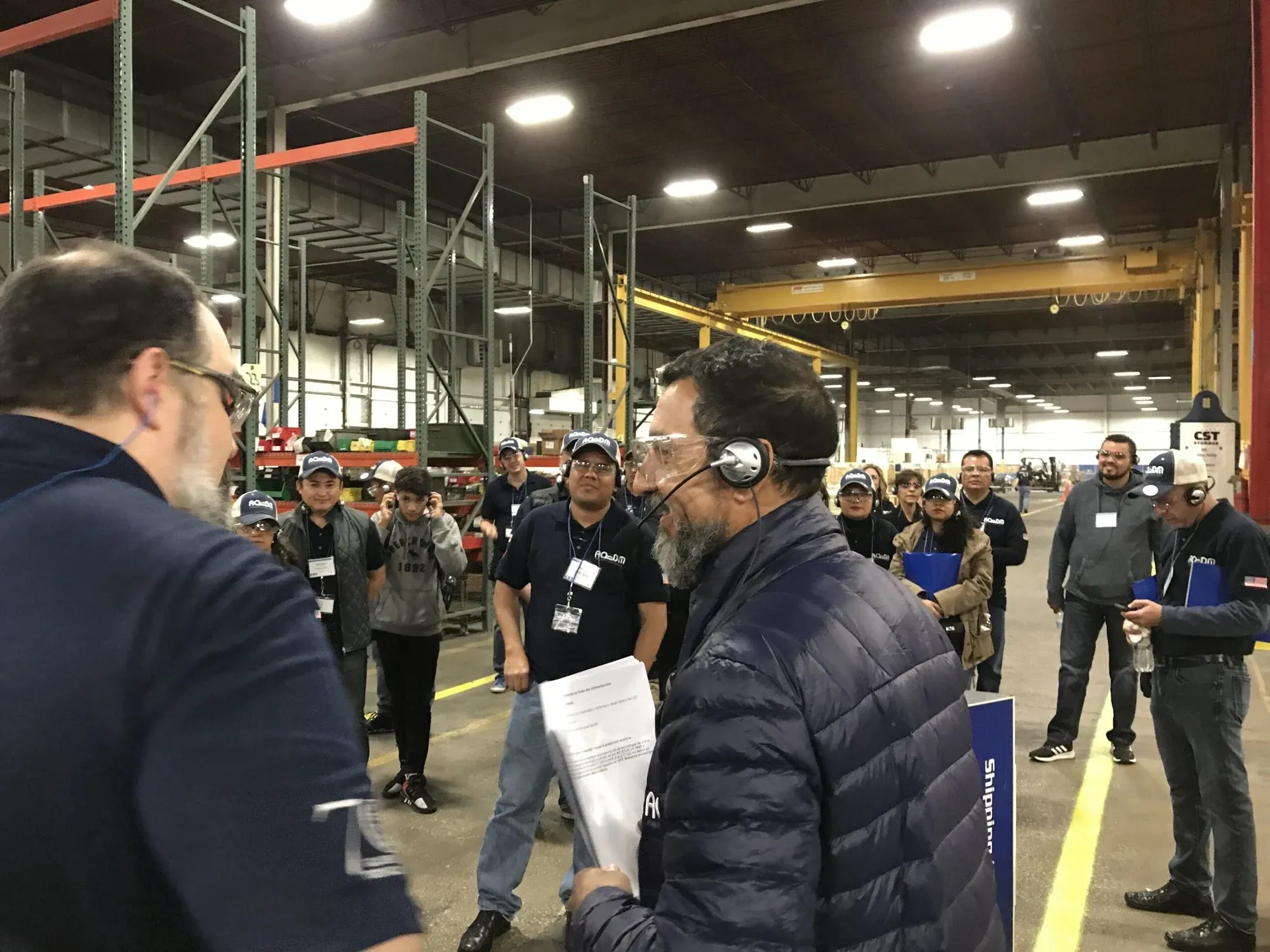 A tour group wearing headsets listens to a guide in a large factory