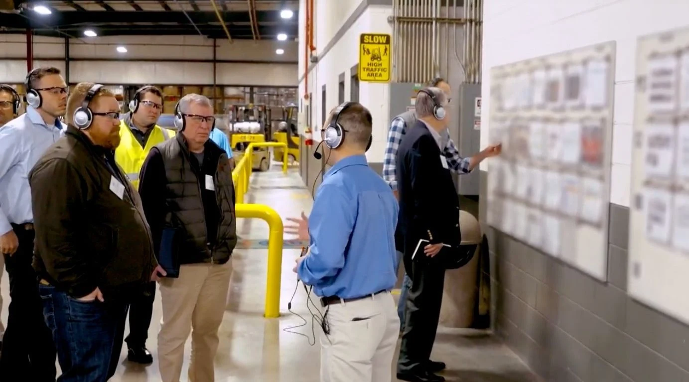 Visitors wearing headsets listening to a guide during a factory tour on the shop floor