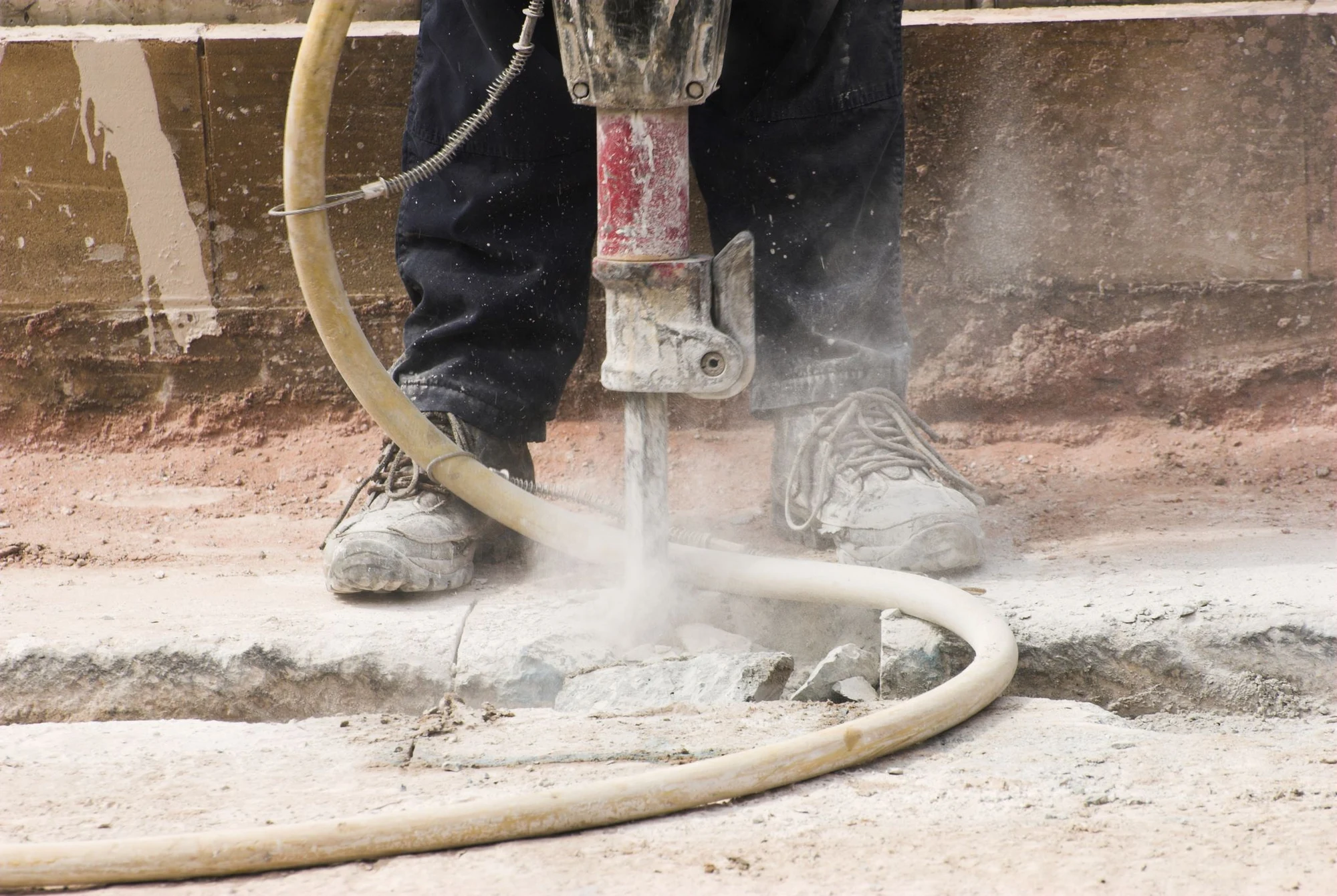 Worker using a jackhammer to break up concrete, sending up dust