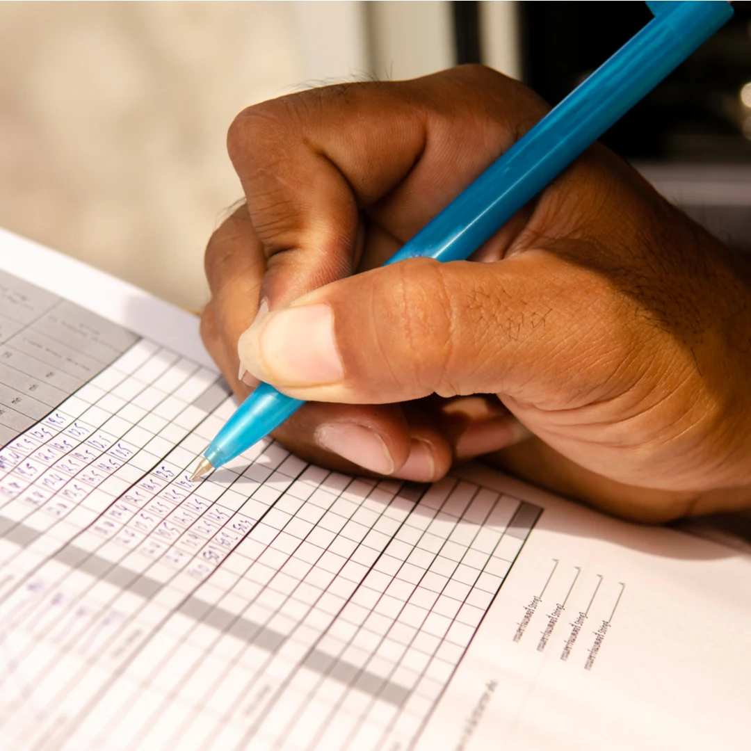 Close-up of a hand writing with a blue pen on a printed checklist
