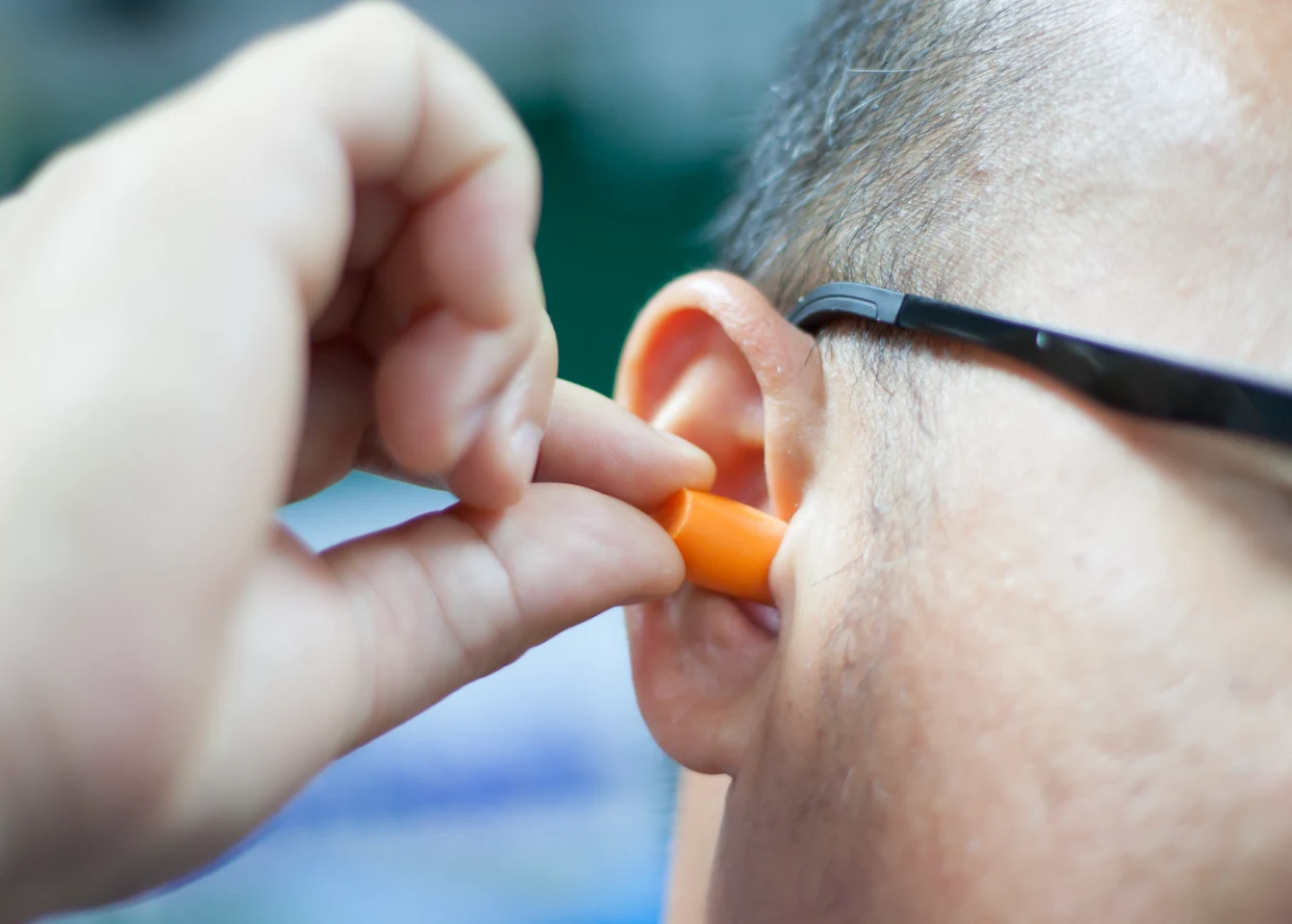 Man in safety glasses inserting an orange foam earplug into his ear