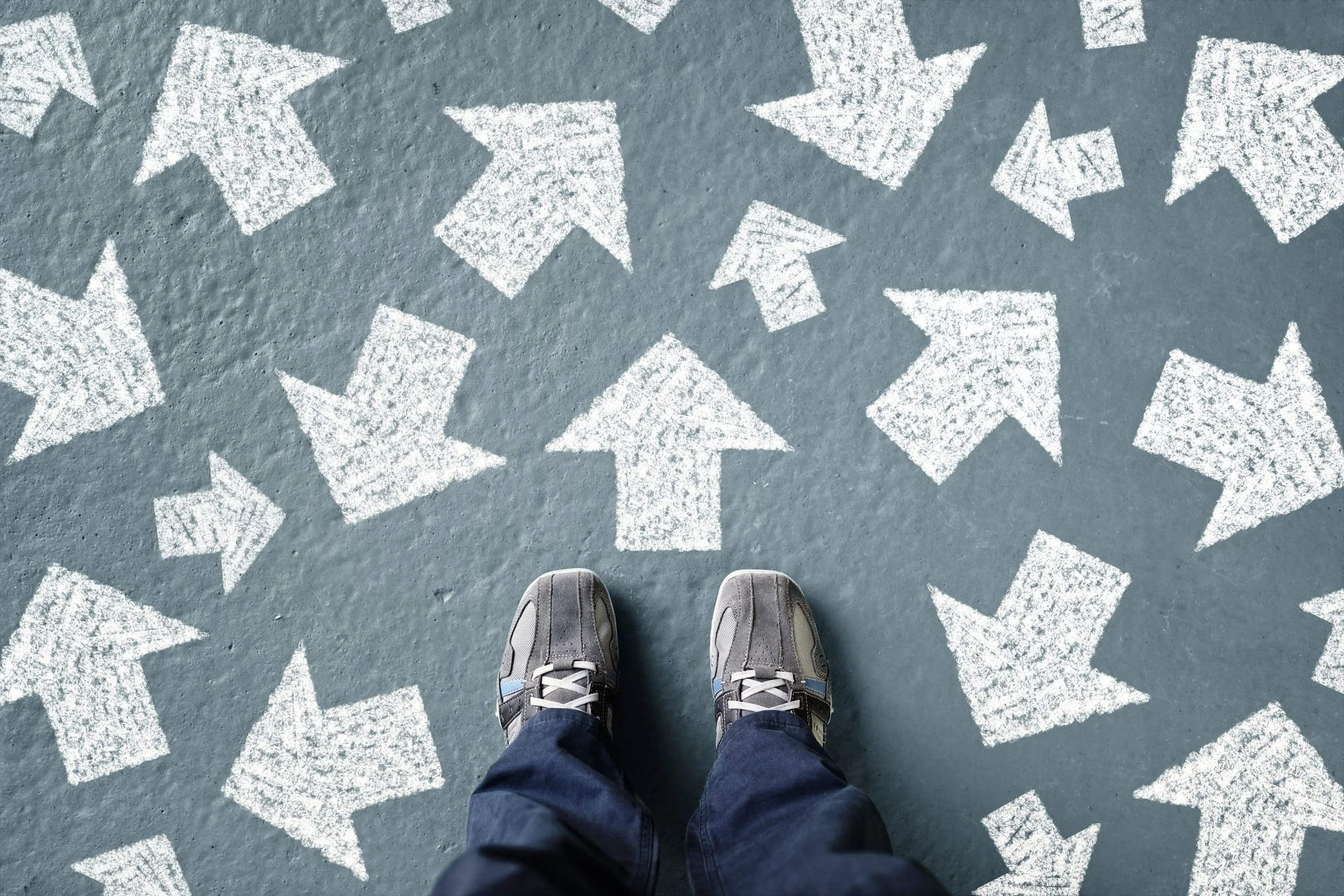 Person standing on pavement covered with white arrows pointing in many different directions