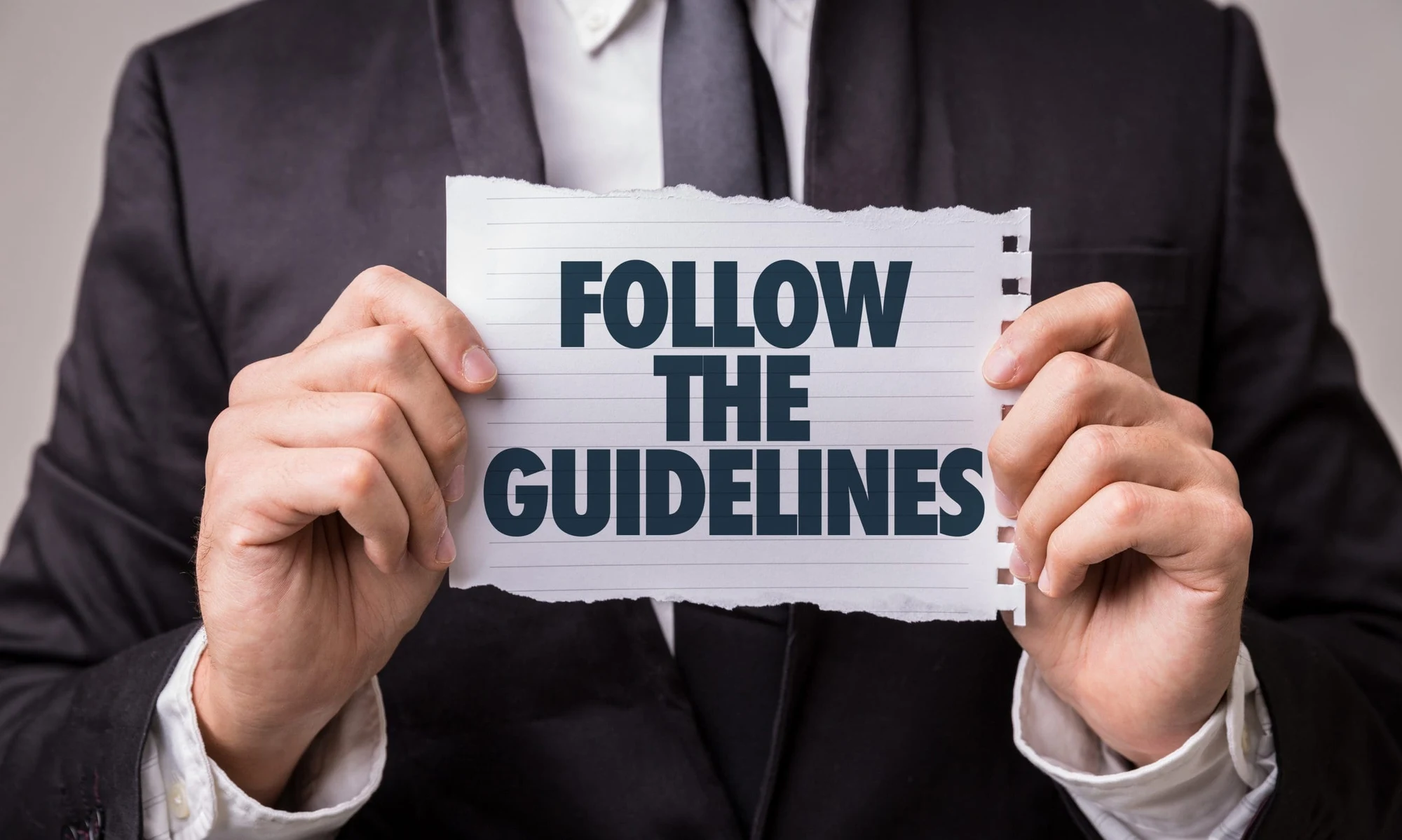 Man in a suit holding a torn paper sign reading Follow the guidelines