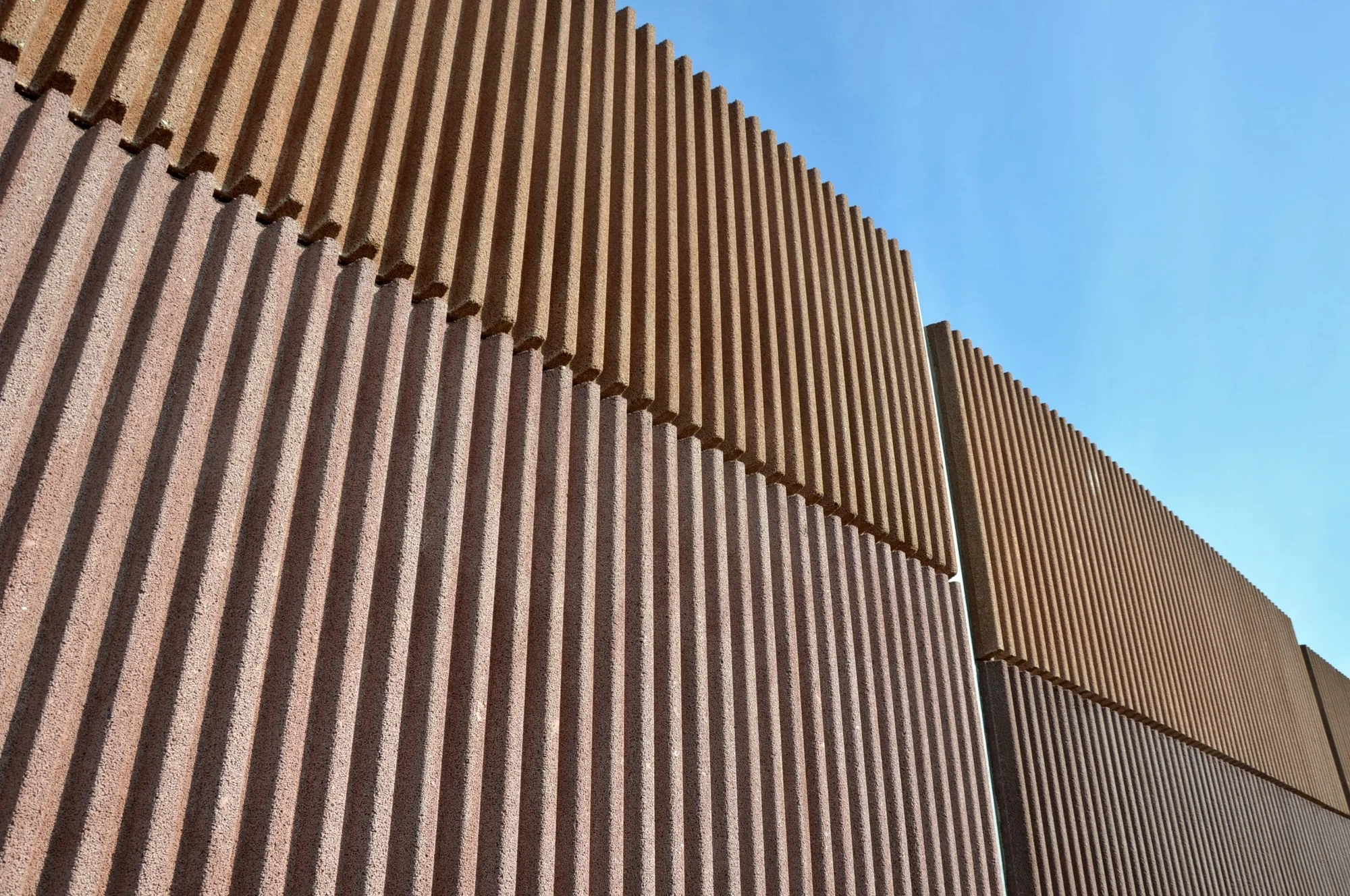Tall slatted exterior wall barrier seen from below against a blue sky