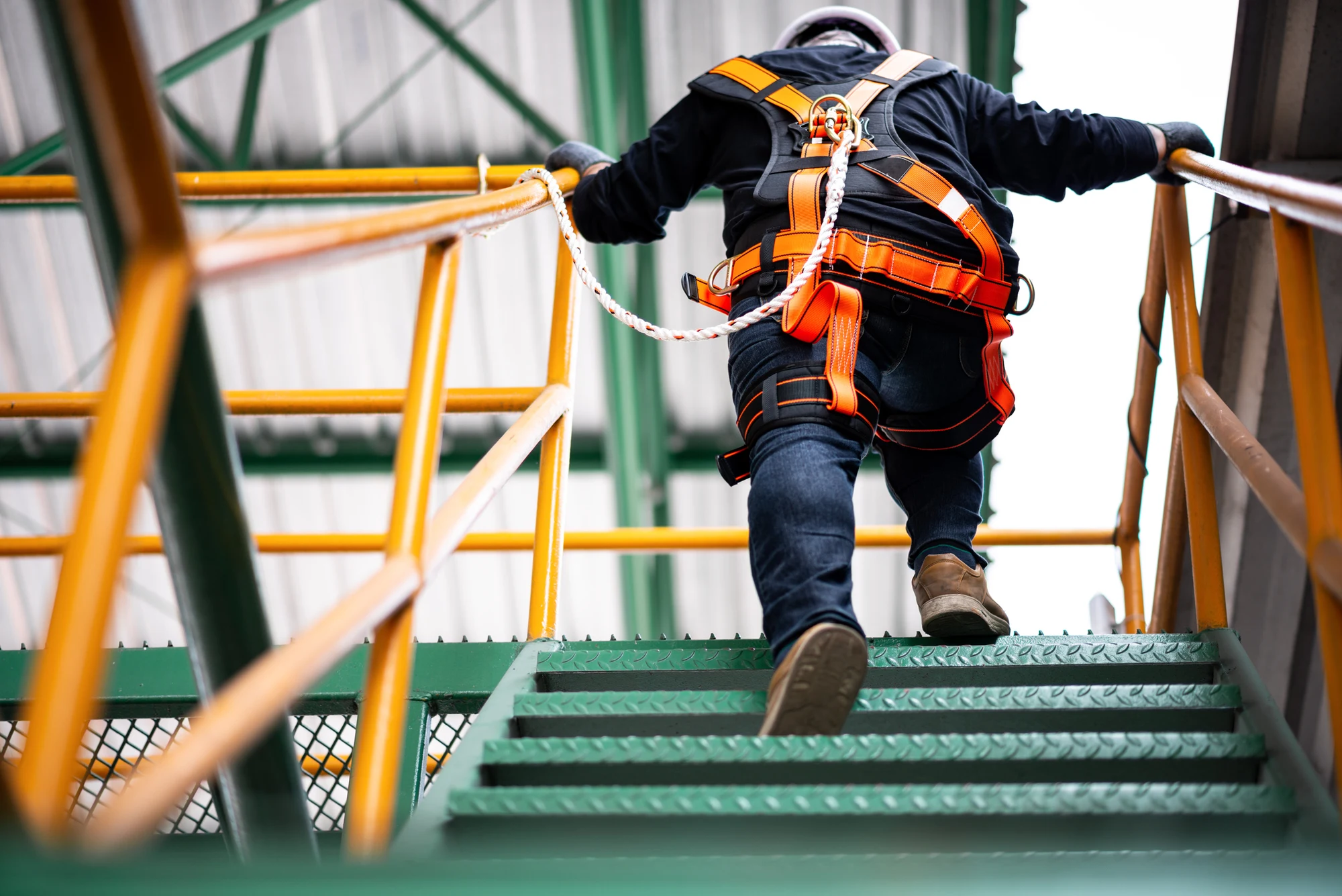 Worker wearing a safety harness climbing industrial metal stairs with yellow railings