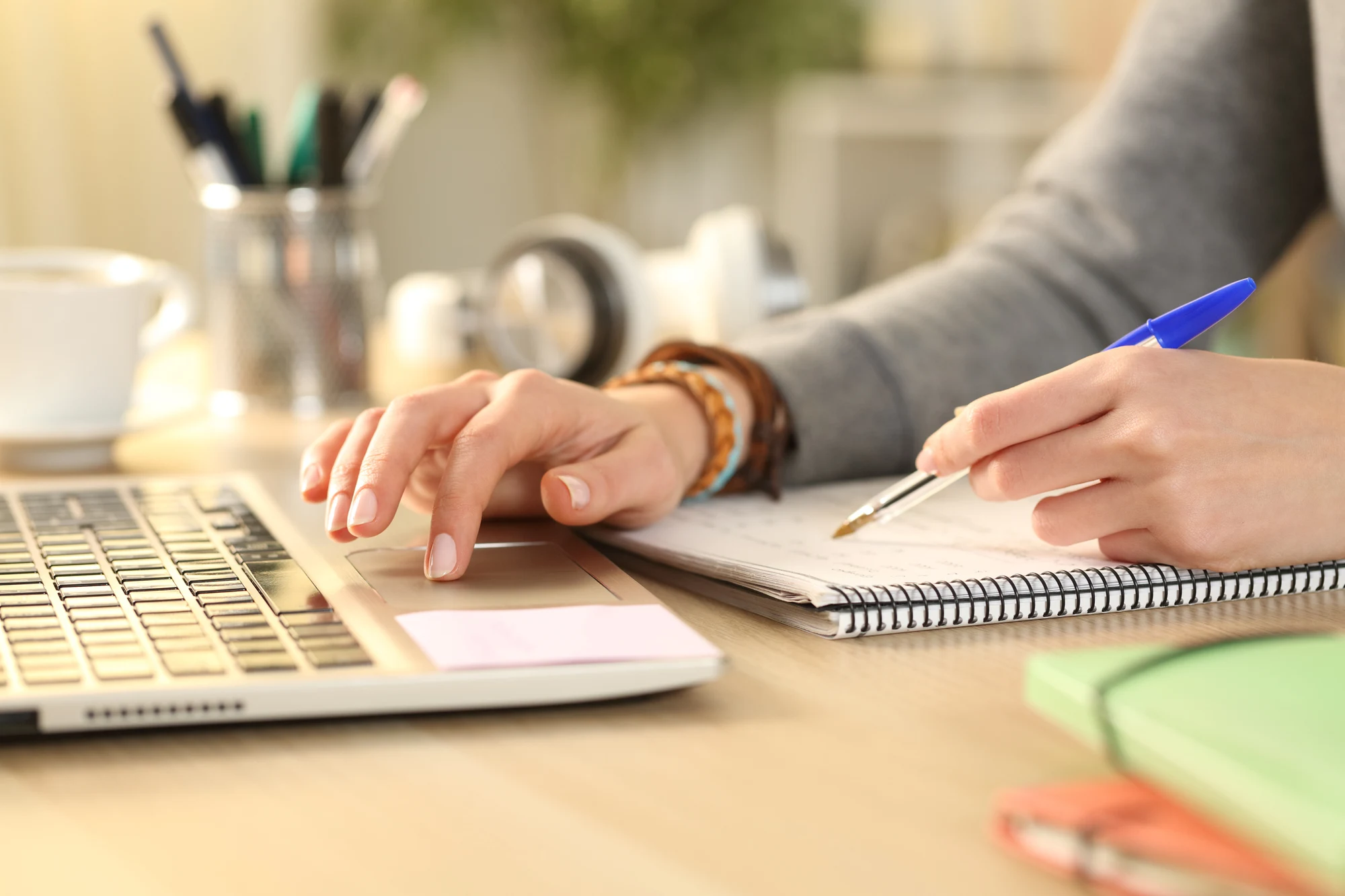 Person typing on a laptop while writing notes in a notebook at a desk