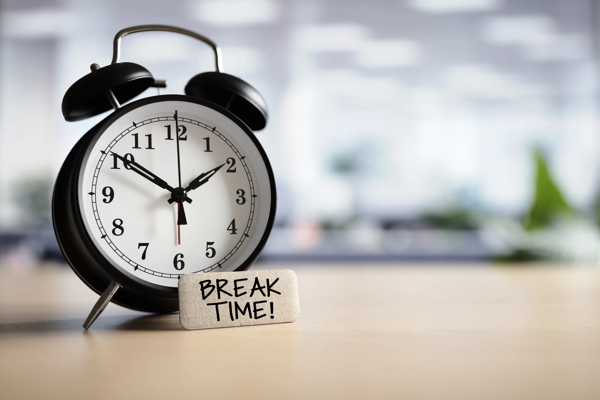 Black alarm clock on a desk next to a sign reading Break Time