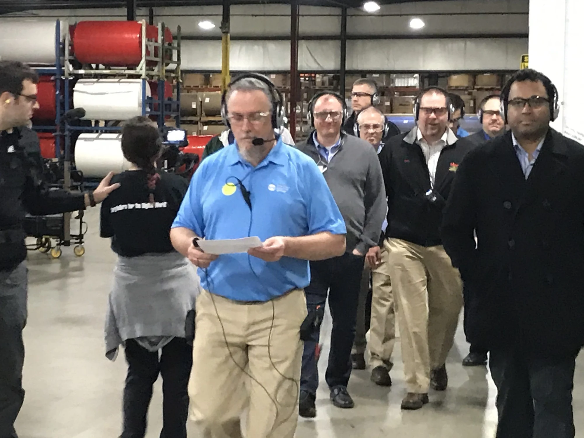 Tour guide in a blue shirt wearing a headset leads a group through a plant