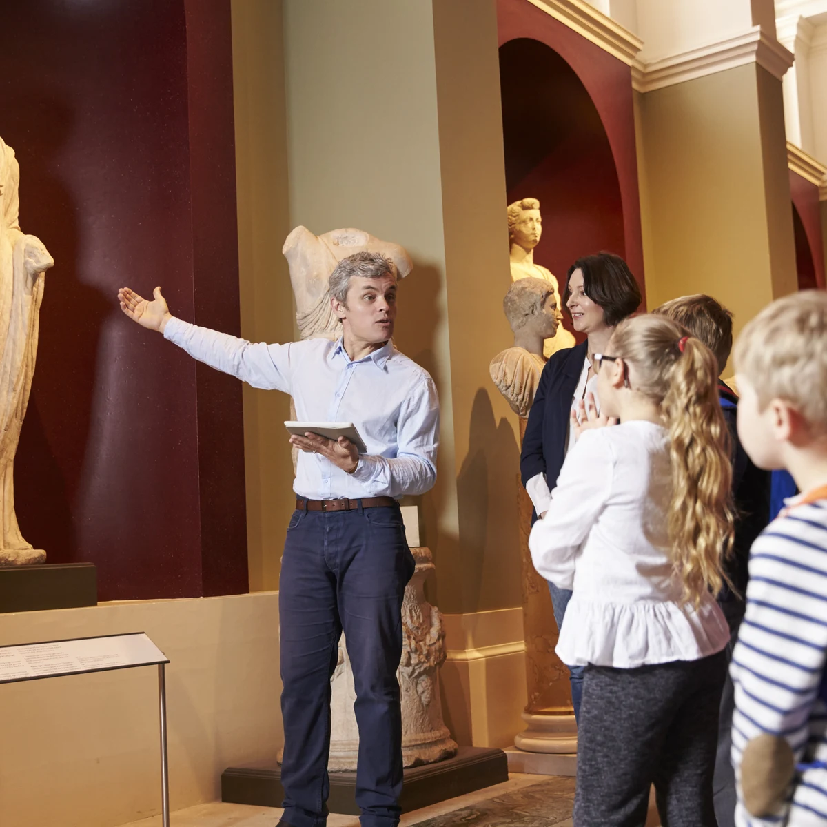 Guide gesturing toward statues while speaking to a small group in a museum